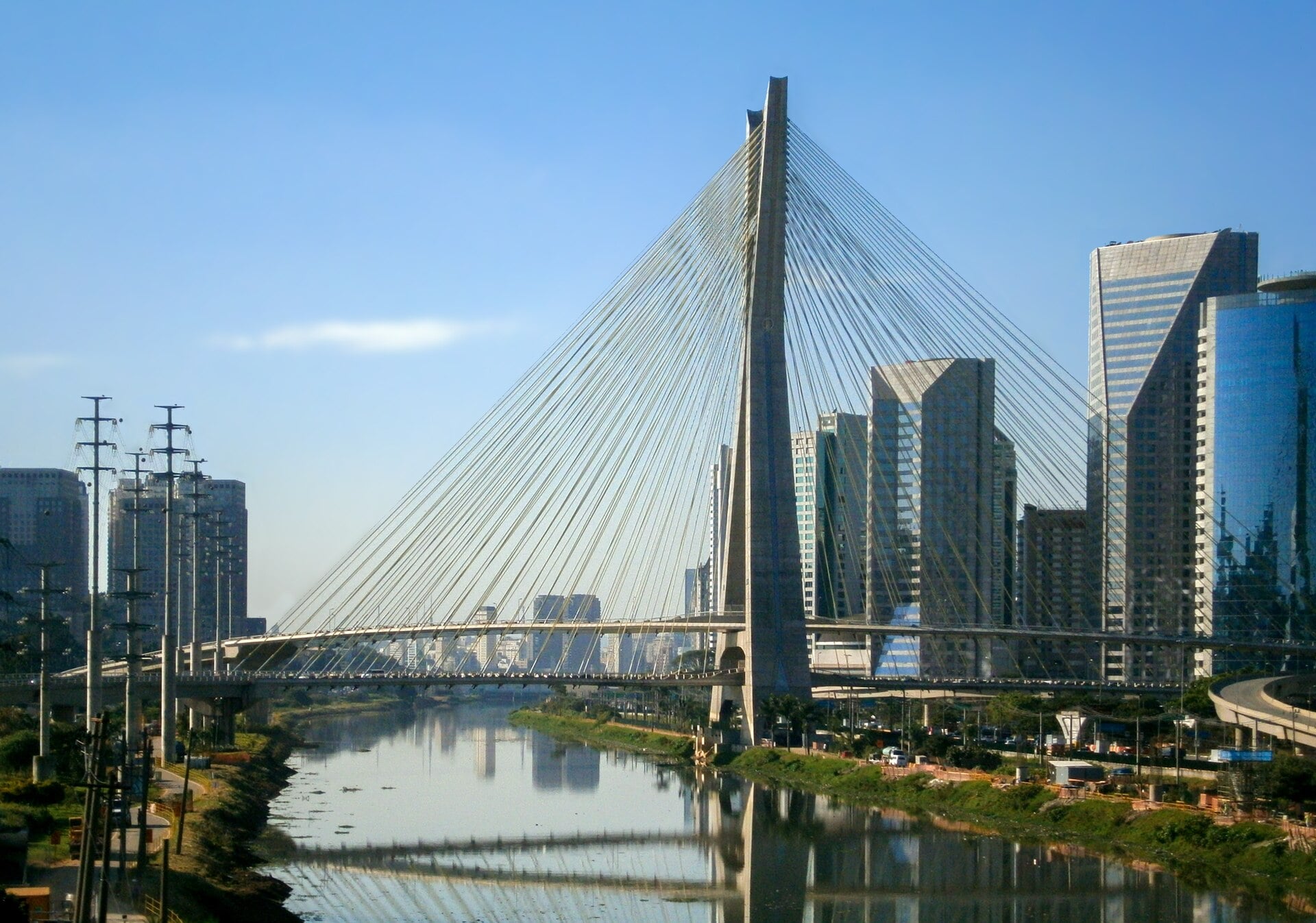 The cable-stayed Octávio Frias de Oliveira bridge over the Pinheiros River with office towers on the right bank under a clear sky