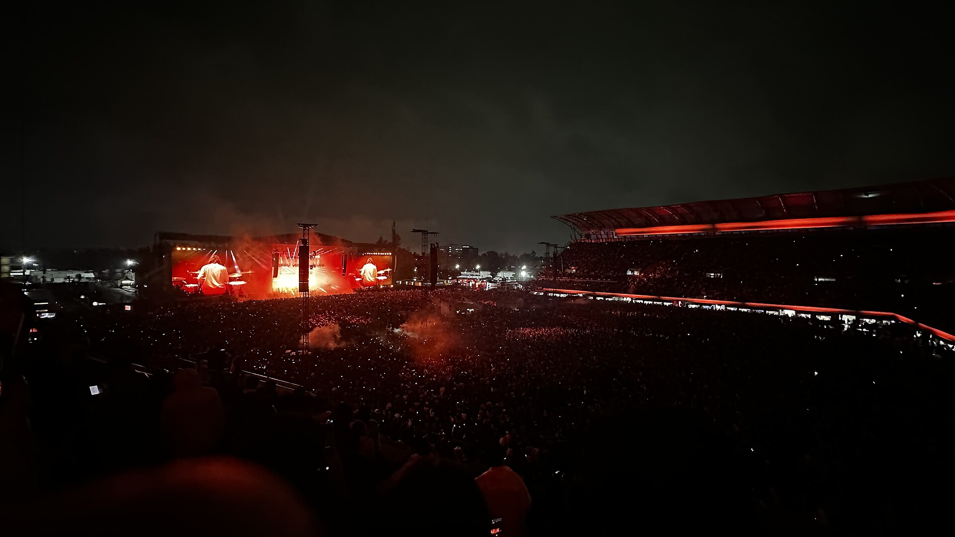 Night concert crowd filling the stands and pitch of Foro Sol, now Estadio GNP Seguros, in Mexico City, with a lit stage and red video screens