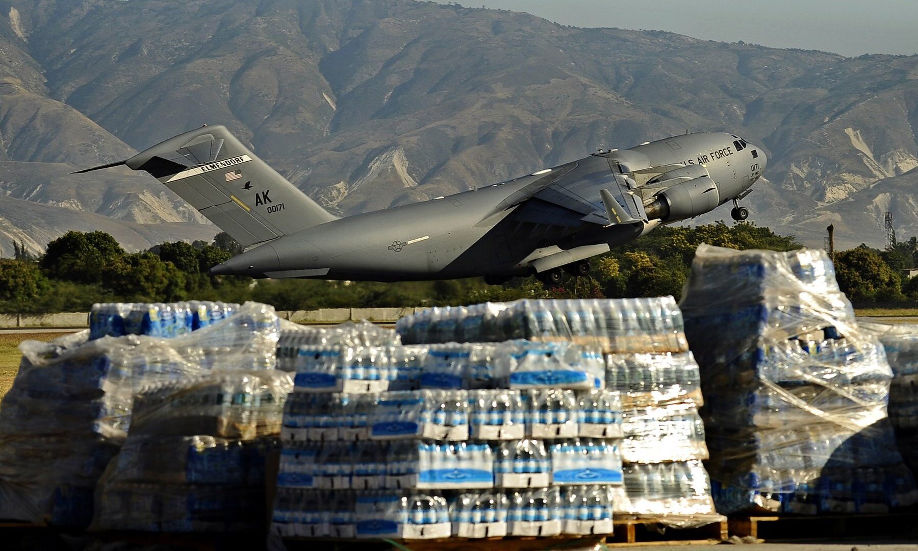 A US Air Force C-17 transport aircraft lifting off from a Haitian airfield behind pallets of bottled water