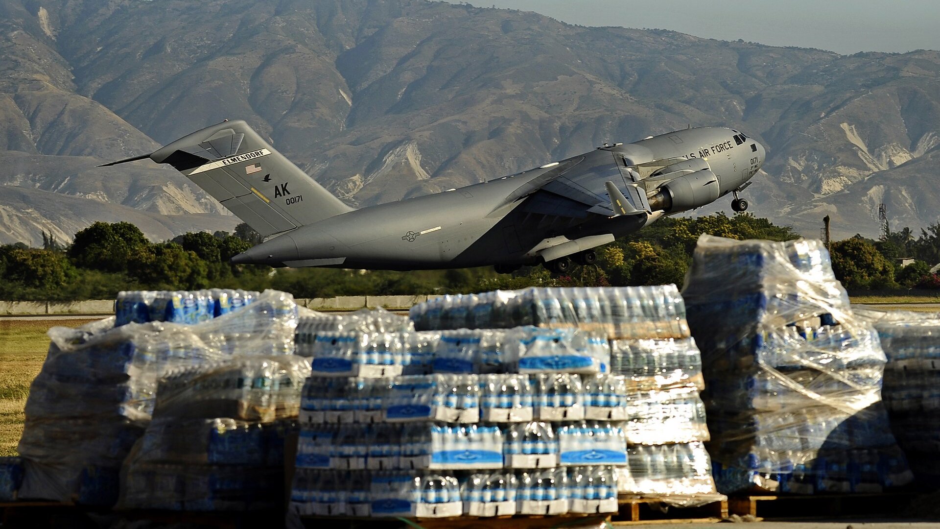 A US Air Force C-17 transport aircraft lifting off from a Haitian airfield behind pallets of bottled water