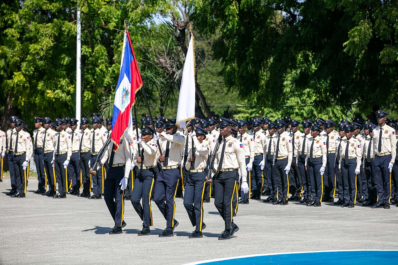 Haitian police cadets in formation behind a colour party carrying the Haitian flag on a parade ground