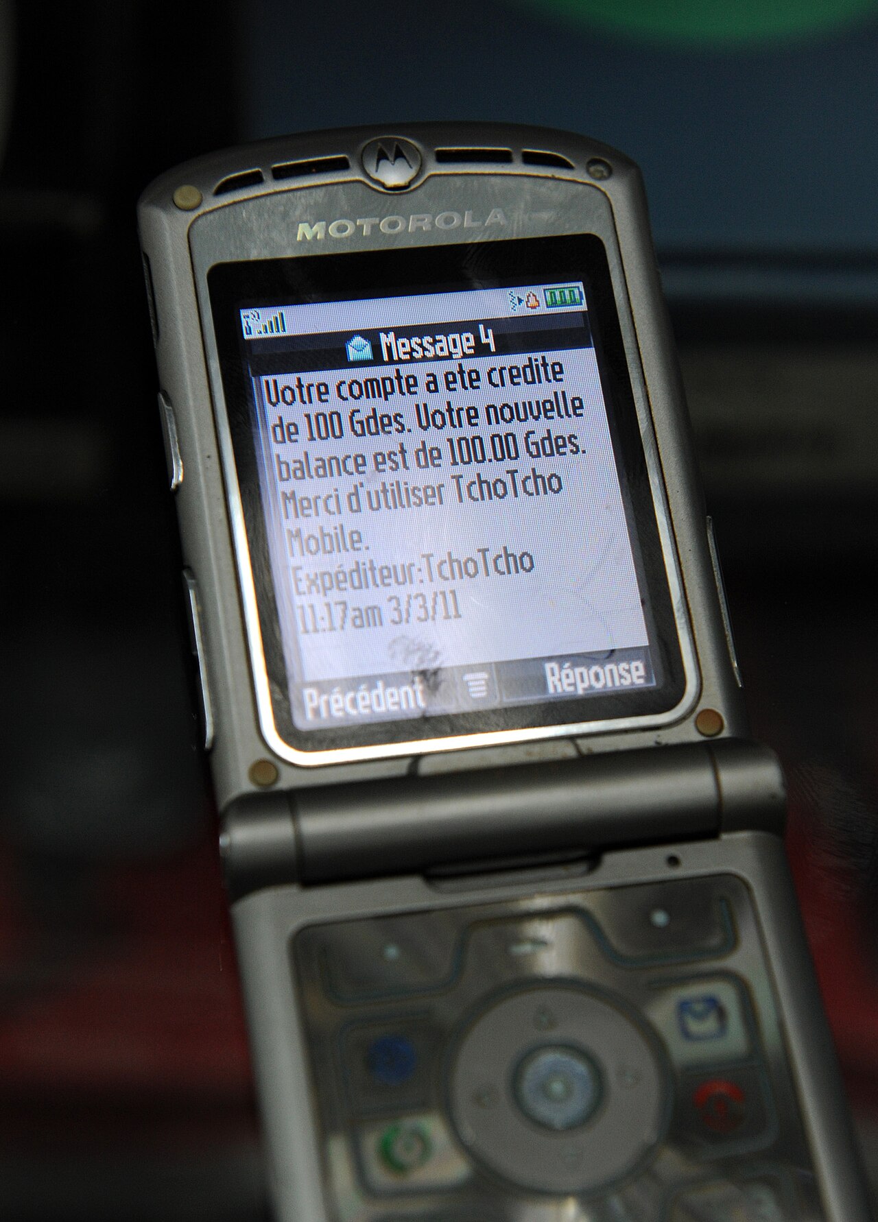 A flip phone screen showing a French text message confirming a mobile money deposit