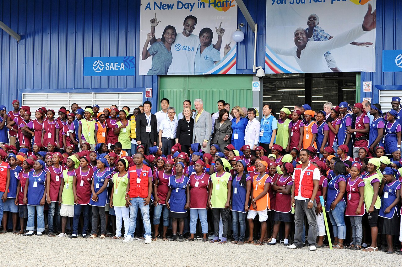 Hundreds of garment workers in coloured aprons and headscarves stand outside a blue factory building at the Caracol Industrial Park.