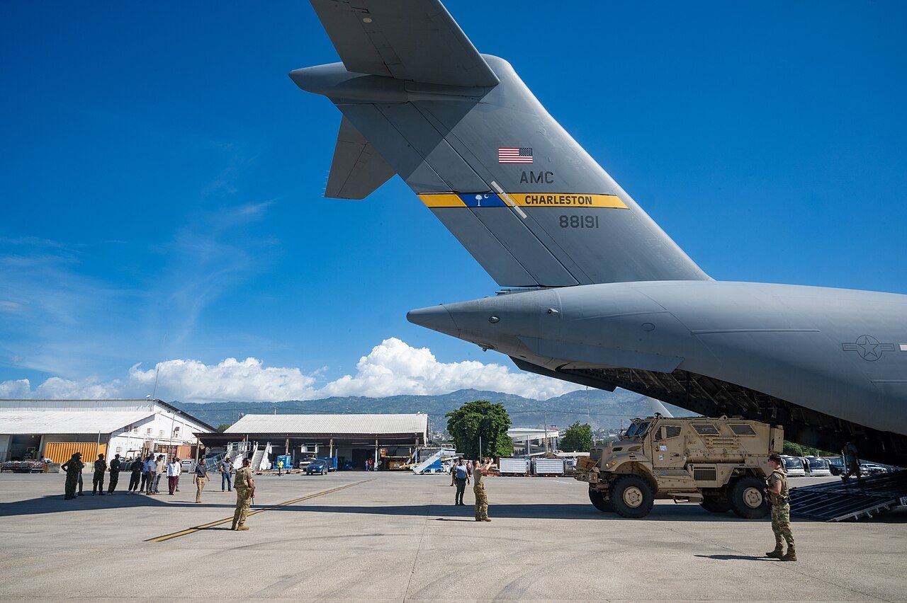 A tan armoured vehicle rolls out of a grey US Air Force cargo plane on the apron of Port-au-Prince airport