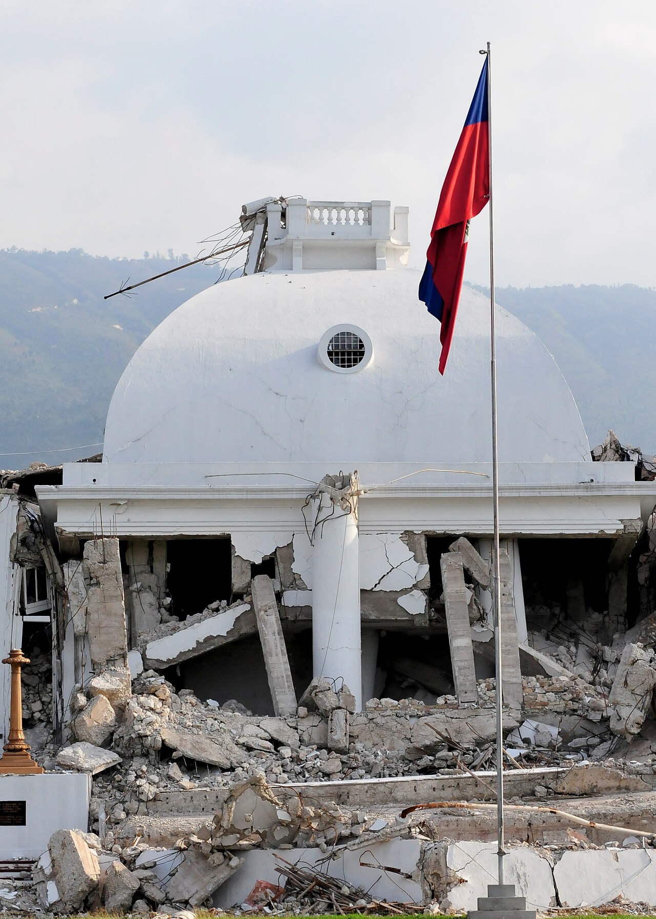 The Haitian flag on a pole in front of the white dome of the National Palace in Port-au-Prince, with rubble in the foreground