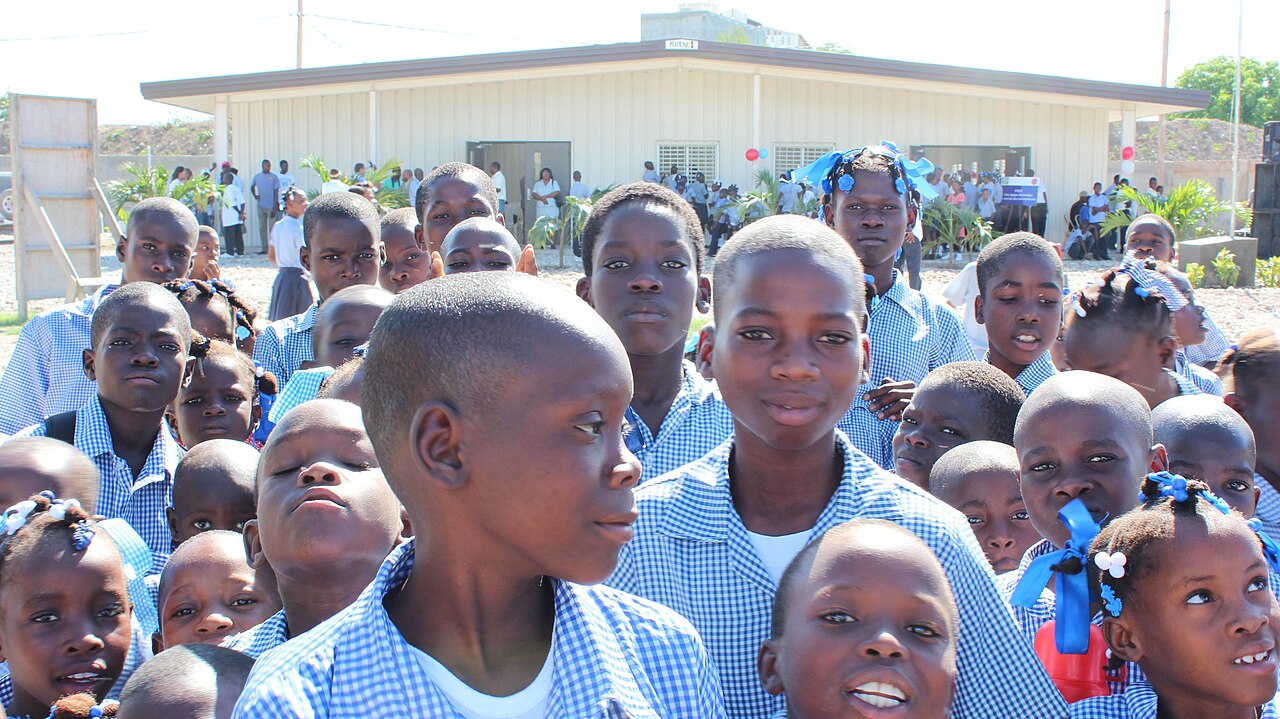 Crowd of Haitian schoolchildren in blue checked uniforms in front of a new school building
