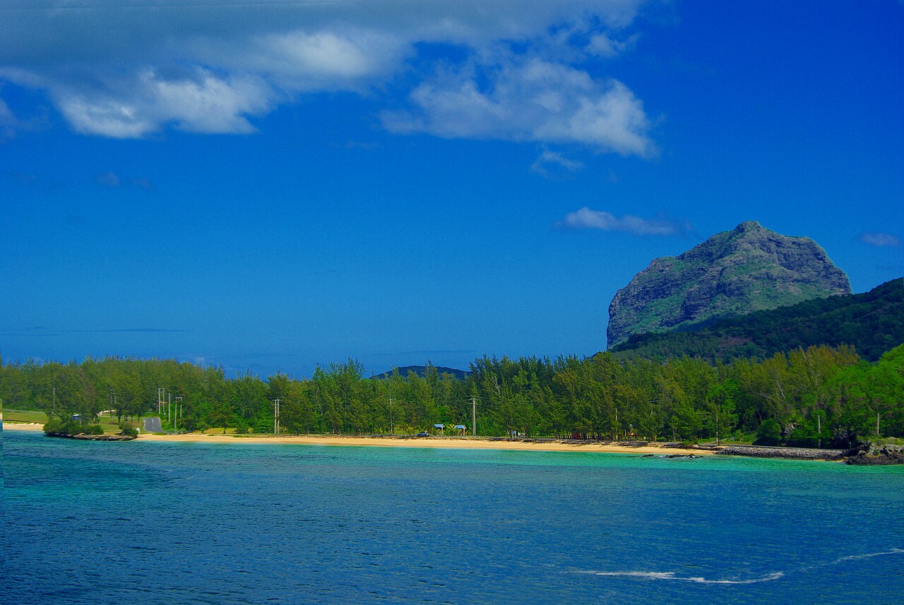 Le Morne Brabant, a green rocky mountain rising beside a sandy beach and turquoise sea on the coast of Mauritius.