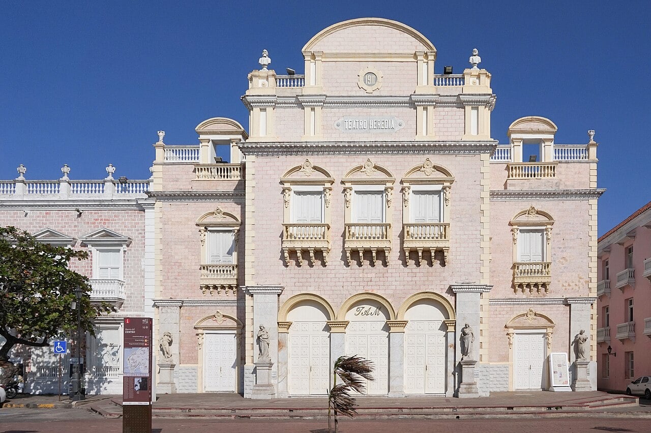 Stone bust on the roofline of the Teatro Adolfo Mejía in Cartagena, Colombia, against a blue sky.