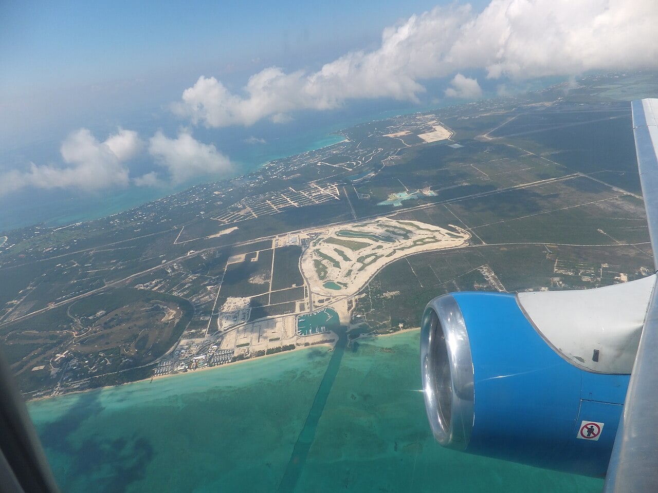 Aerial view from a plane window of the coast of New Providence, with the Albany golf course and marina under construction beside turquoise water.