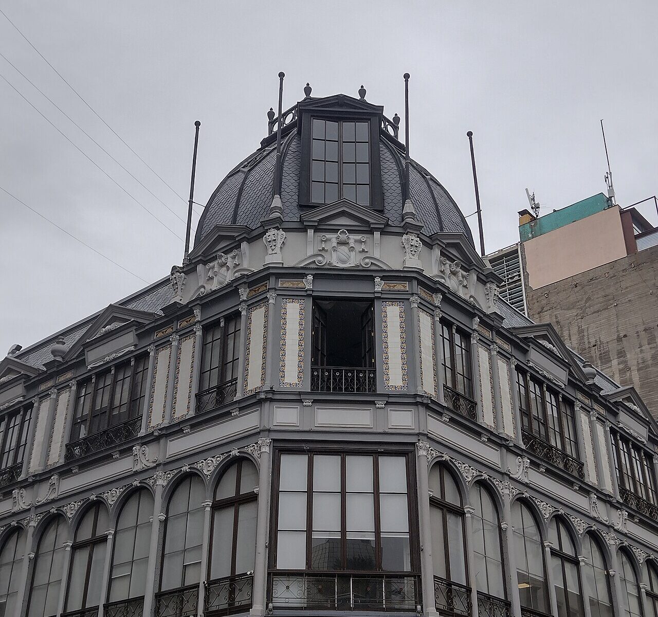Grey and cream corner building with a slate dome and tiled balconies in central Santiago, Chile, with a pharmacy sign at street level