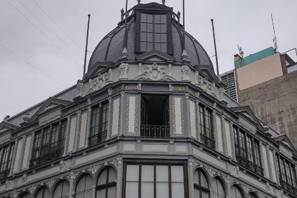 Grey and cream corner building with a slate dome and tiled balconies in central Santiago, Chile, with a pharmacy sign at street level