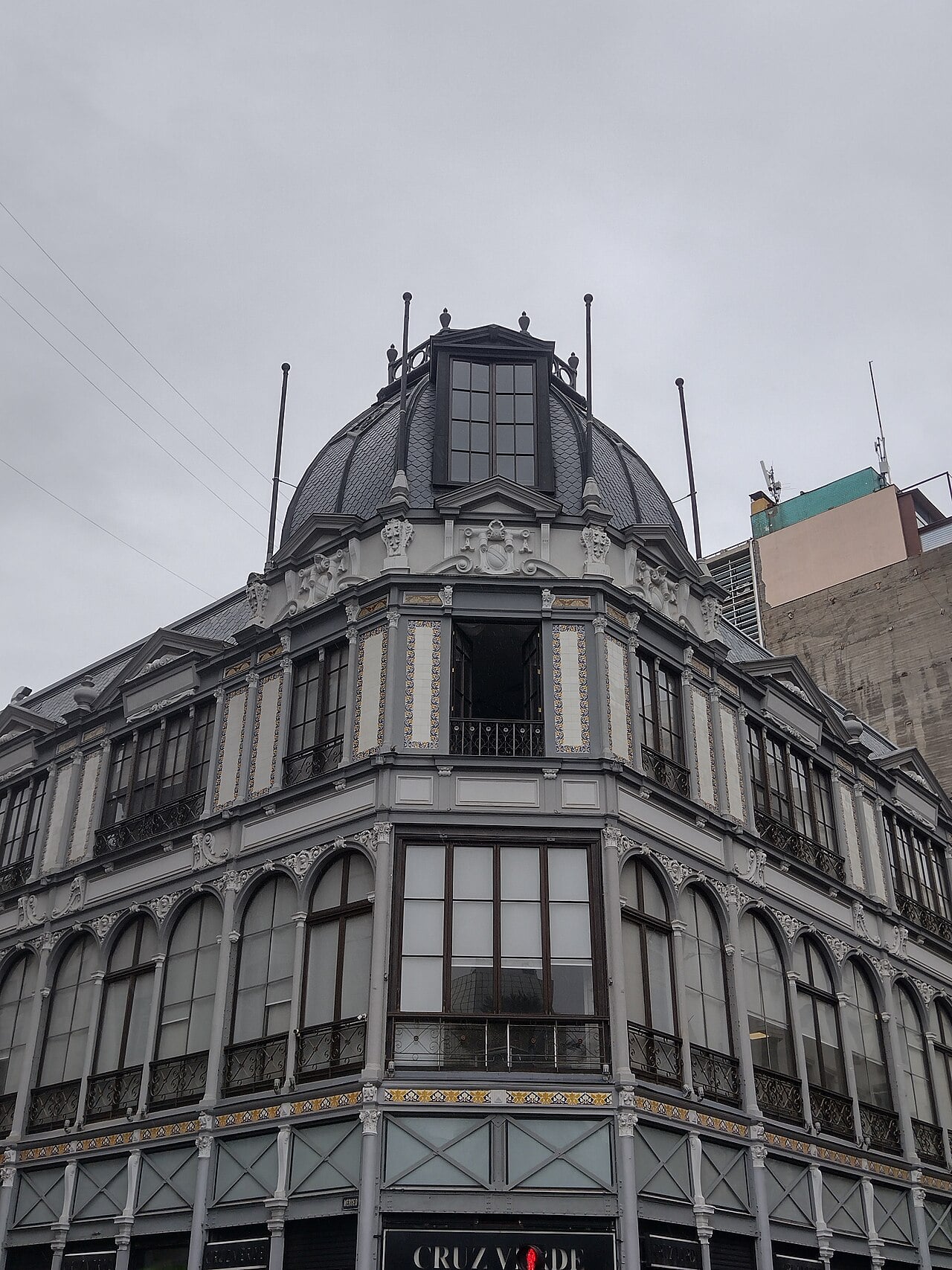 Grey and cream corner building with a slate dome and tiled balconies in central Santiago, Chile, with a pharmacy sign at street level