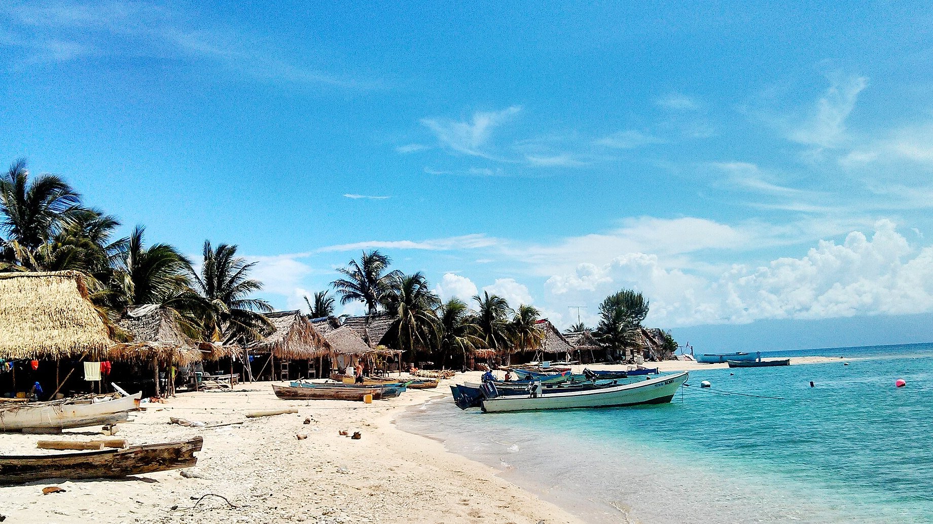 Thatched huts and fishing boats on the white sand beach of Chachahuate cay in the Cayos Cochinos, Honduras