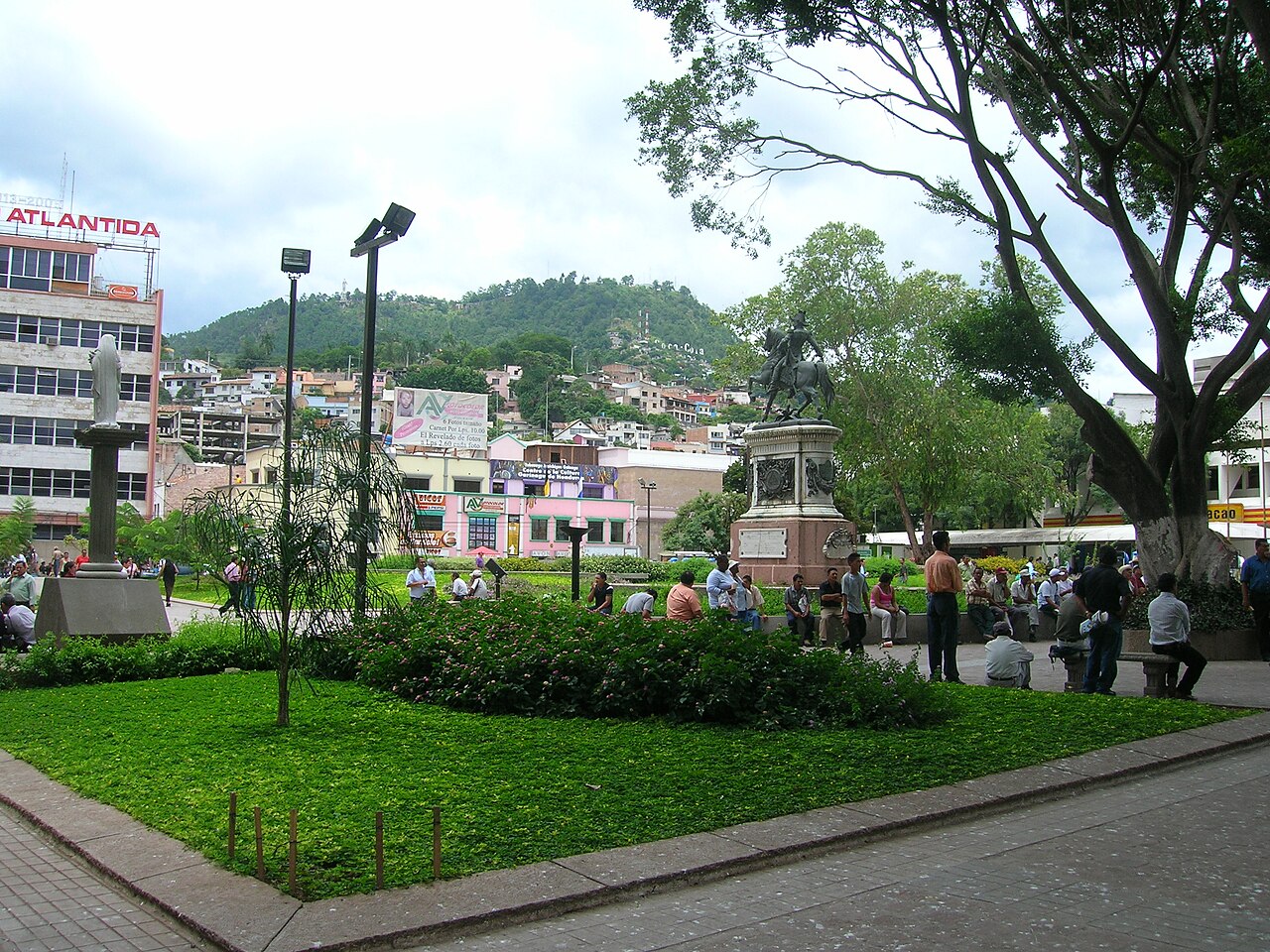 Plaza Central in Tegucigalpa with an equestrian statue, lawns, people on benches and a green hill behind the city
