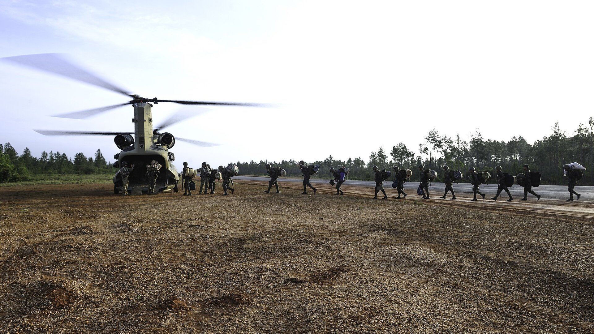 Honduran soldiers with packs walking in a line toward a US military Chinook helicopter on an airstrip at Mocorón, Honduras
