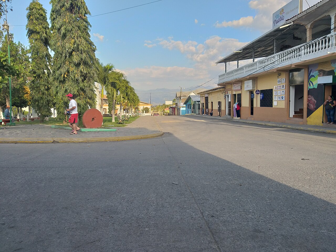 Main street and tree-lined plaza in downtown La Labor, Ocotepeque, Honduras, with shops and mountains in the distance