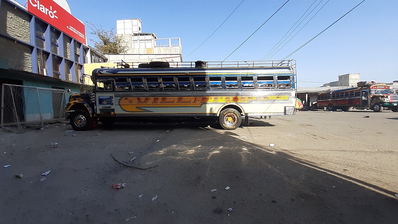 A painted former school bus, known as a chicken bus, parked at a dusty bus terminal in Huehuetenango, Guatemala