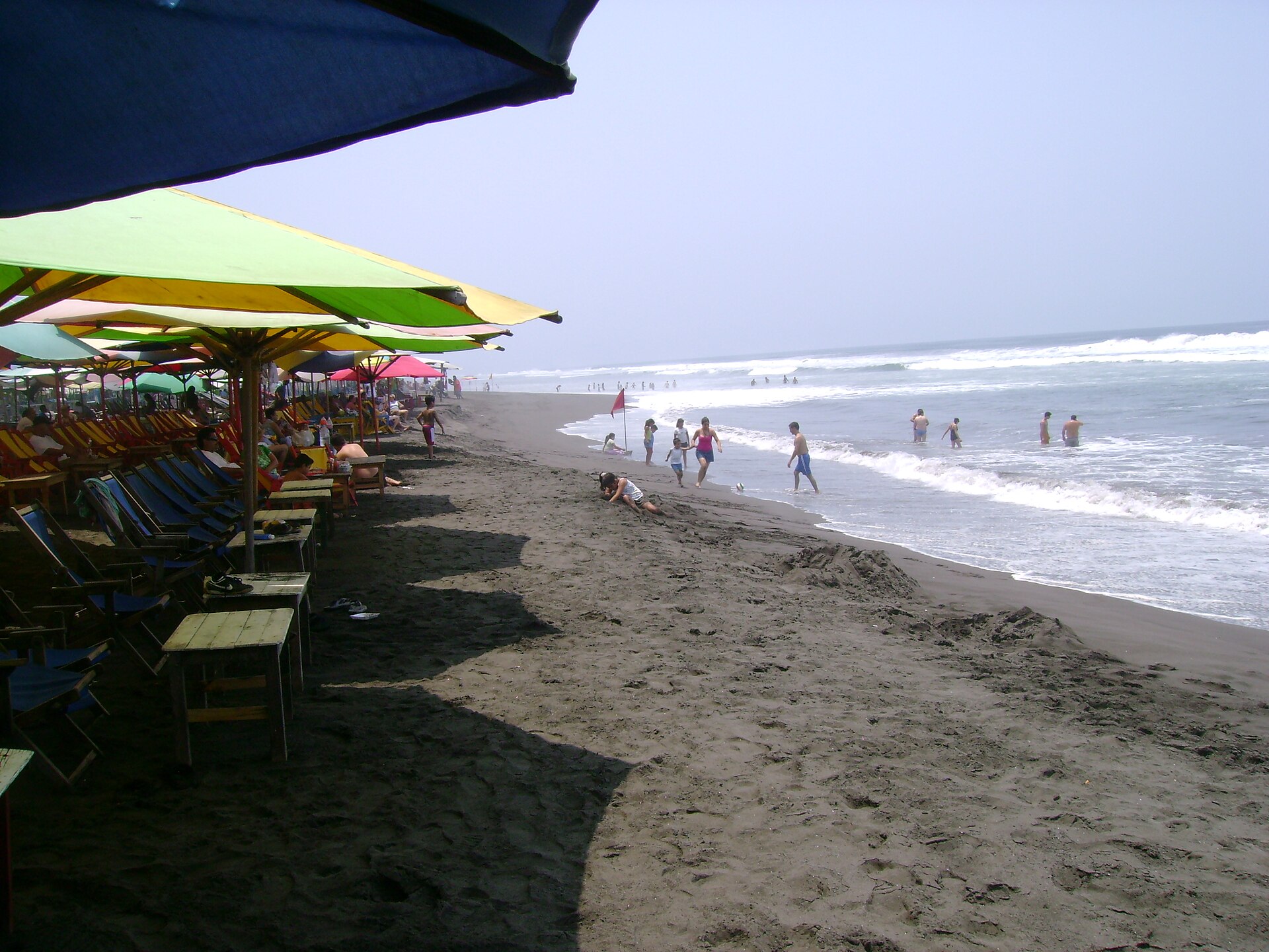 Beach umbrellas, loungers and bathers on the dark sand of Cuyutlán beach in Armería, Colima, Mexico