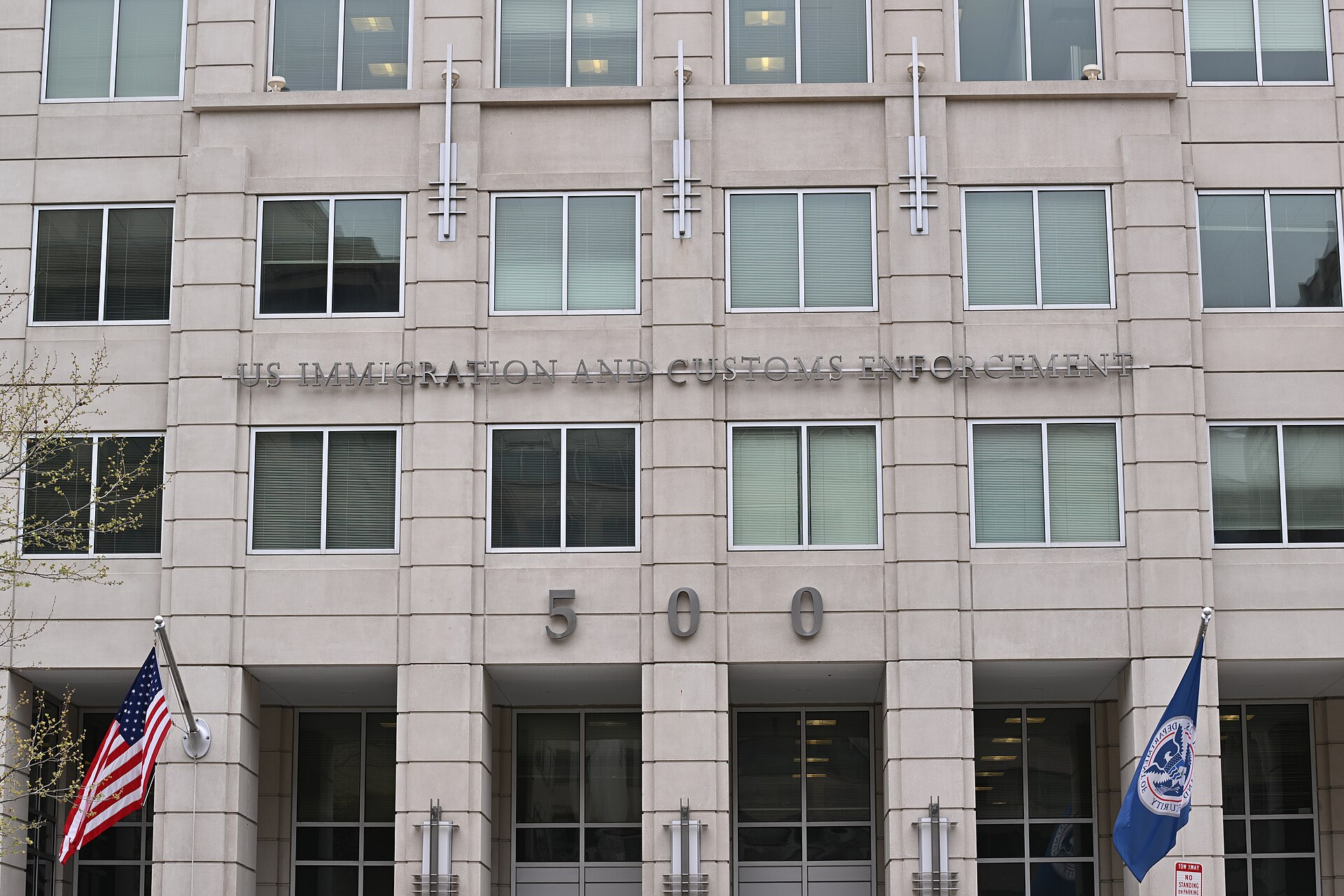 Facade of the U.S. Immigration and Customs Enforcement headquarters building in Washington, DC, with a U.S. flag and a Department of Homeland Security flag
