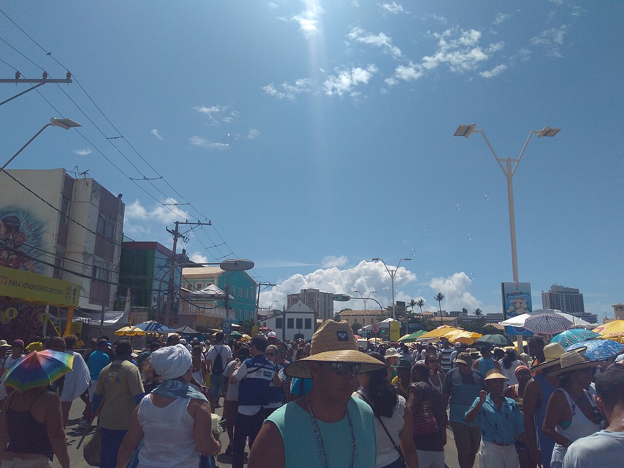 A street in Rio Vermelho, Salvador, crowded with people, many in white and sun hats, on the day of the Iemanjá festival in 2019.