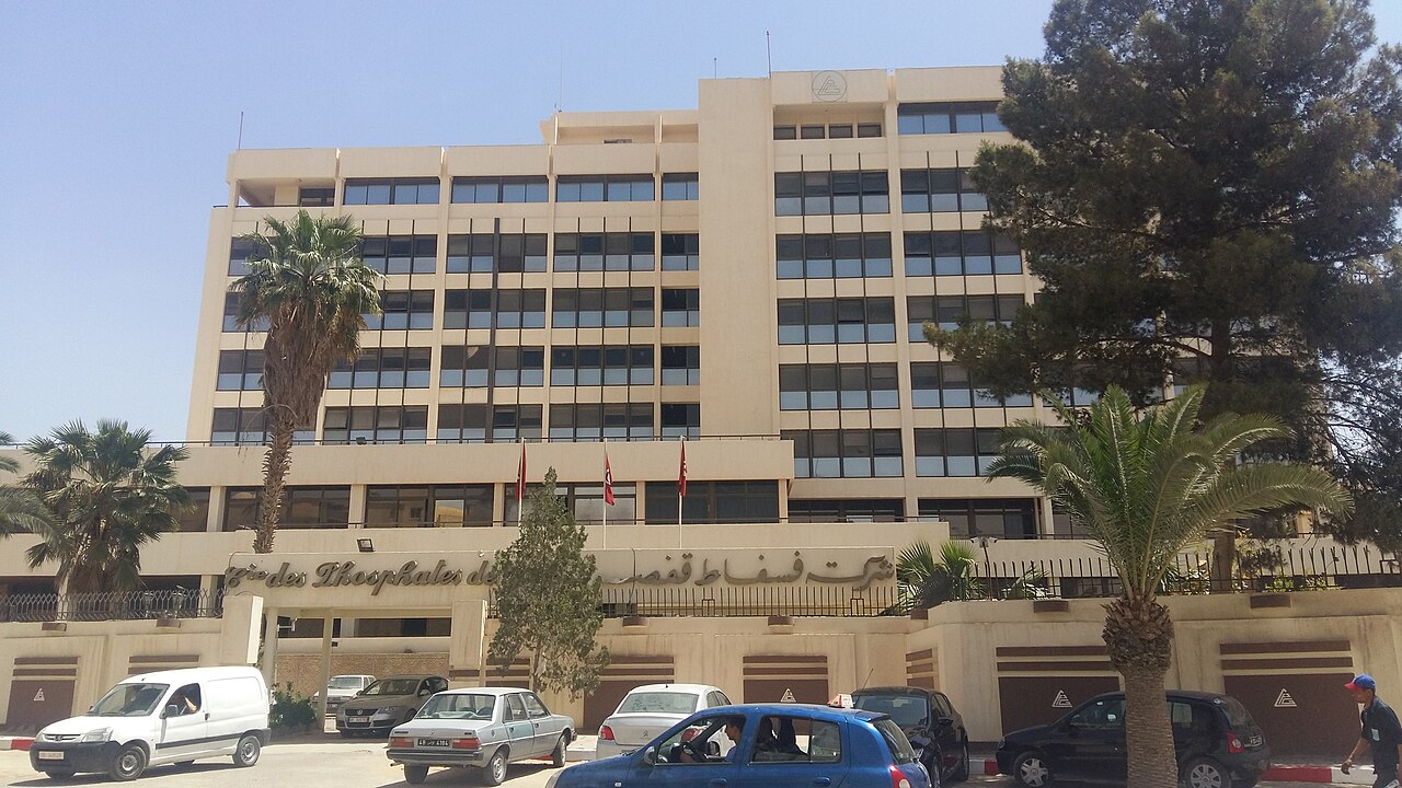 Multi-storey office building of the Compagnie des Phosphates de Gafsa with Tunisian flags, palm trees and parked cars