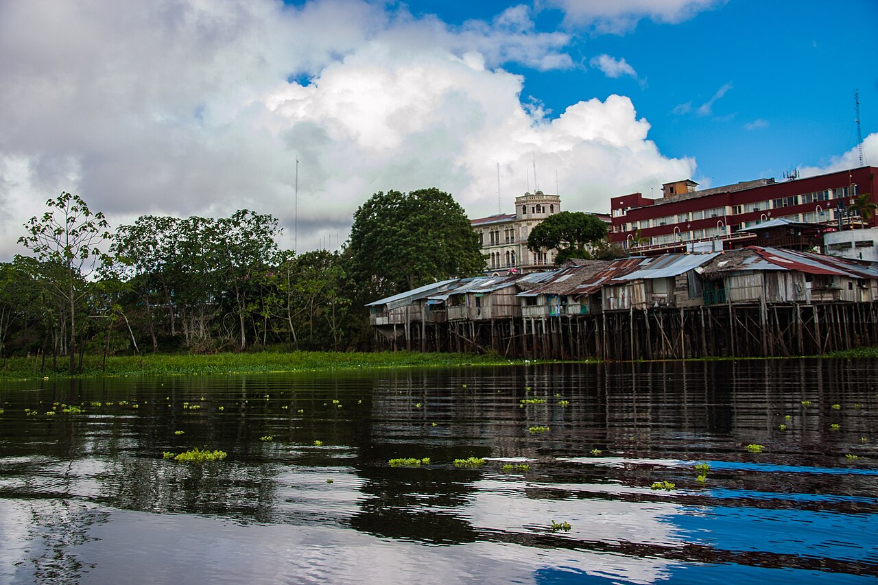 Wooden stilt houses and older buildings line the Itaya River waterfront in Iquitos under a cloudy sky