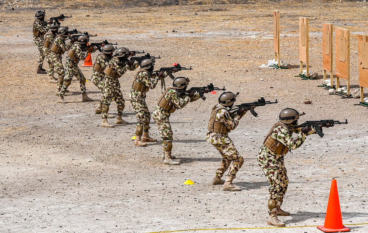 Nigerian Army soldiers in camouflage and helmets aim rifles in a line during a live-fire training exercise