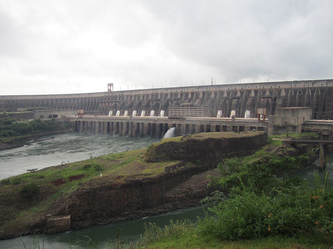 The long concrete buttress wall of the Itaipú Dam and its powerhouse beside the Paraná River under grey skies