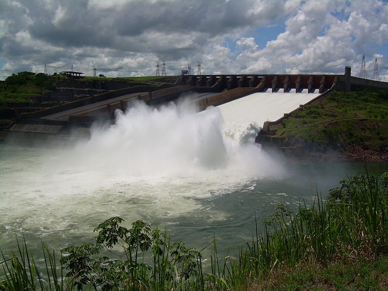 White water pouring down the Itaipú spillway into the Paraná River under a cloudy sky