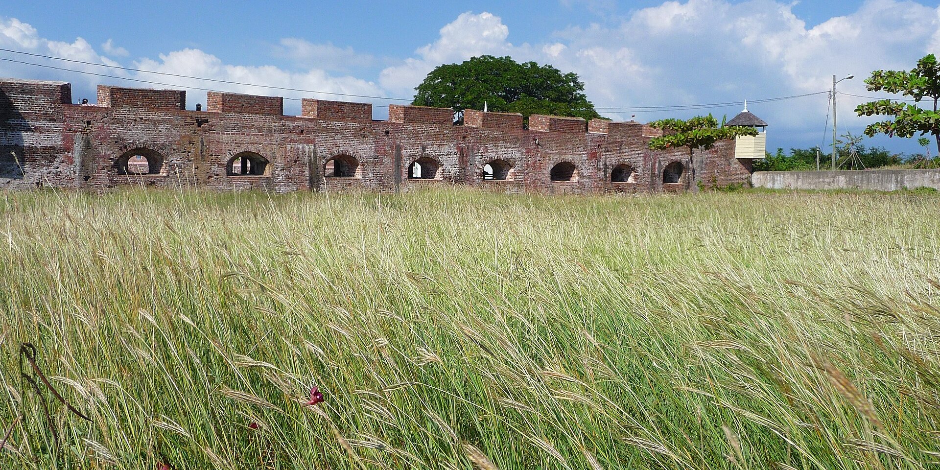 Brick walls and gun embrasures of Fort Charles at Port Royal, Jamaica, above a field of tall grass