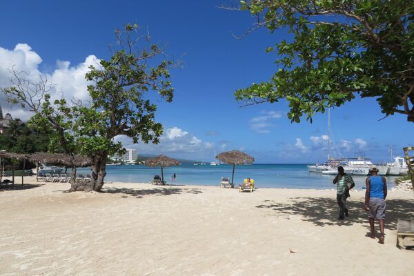 White sand beach and calm turquoise bay at Ocho Rios, Jamaica, with a hotel tower and catamarans in the distance