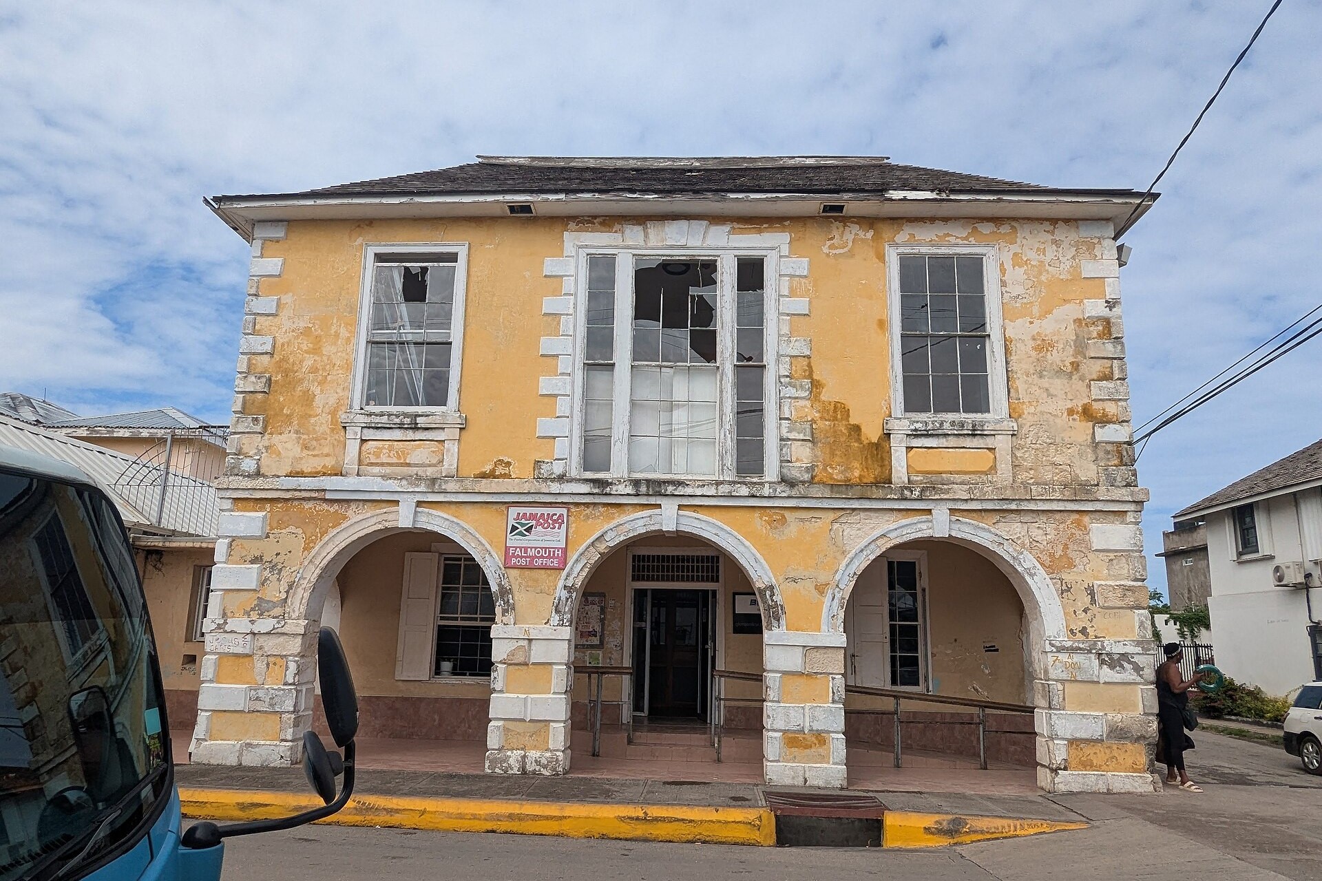 Two-storey yellow colonial building with an arched ground floor, a Jamaica Post sign and broken upper-floor windows in Falmouth, Jamaica
