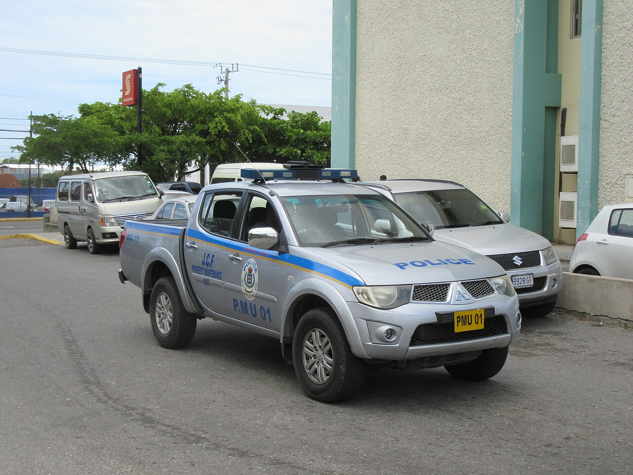 Silver Jamaica Constabulary Force pickup truck marked Police with blue stripes parked beside a building