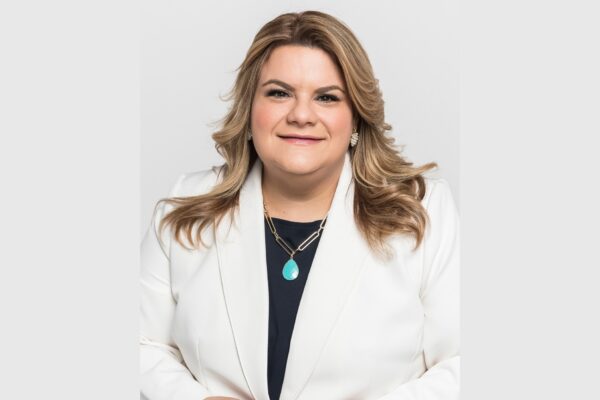Puerto Rico Governor Jenniffer González-Colón smiling in a white blazer against a light grey studio background