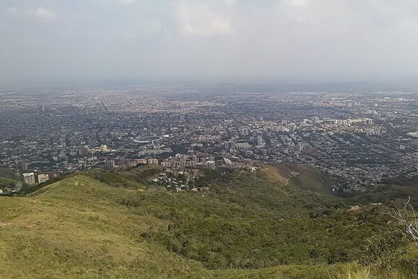 Hazy view over the city of Cali spreading across the flat Cauca River valley, seen from a green hillside on the western edge of the city.