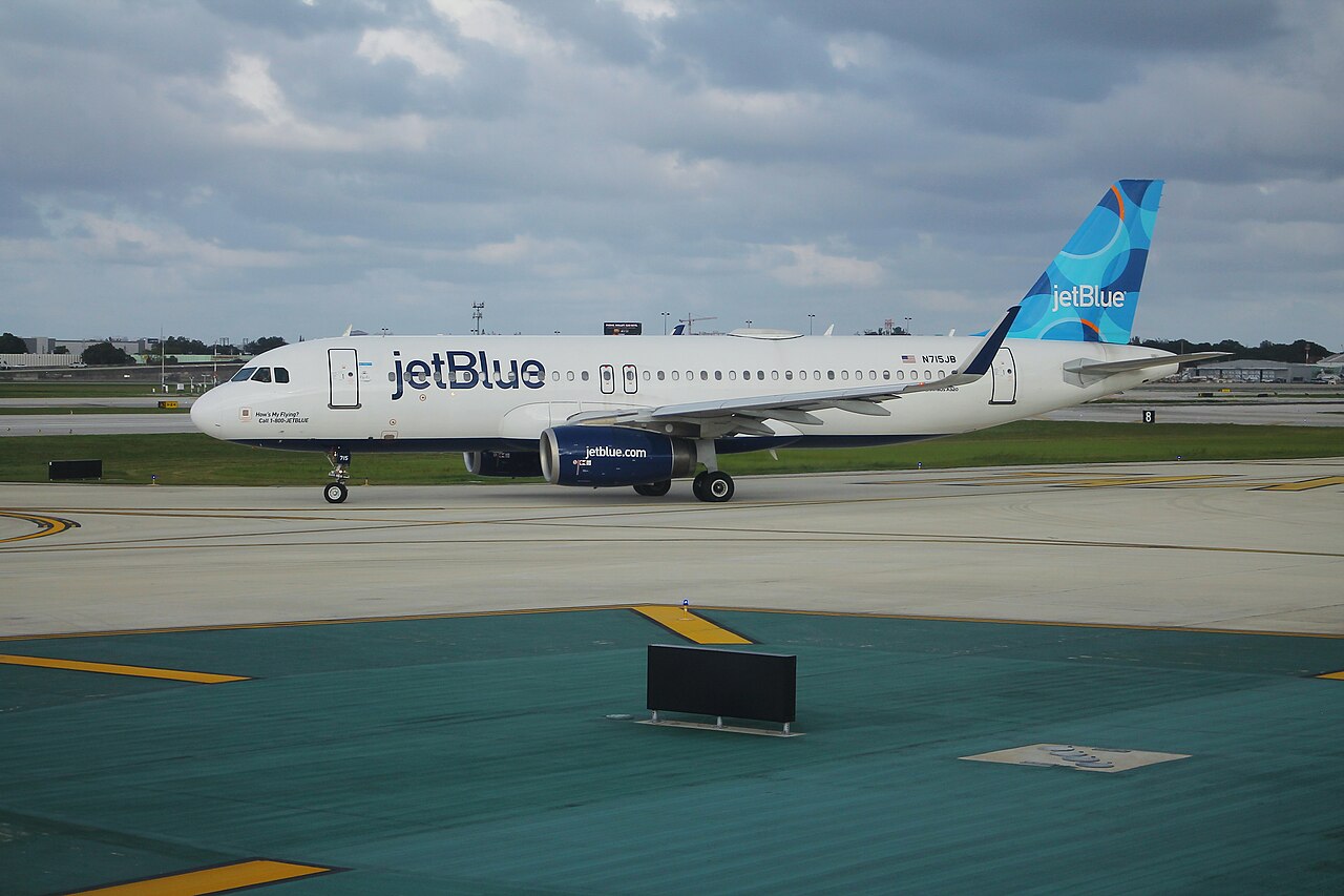 A white JetBlue Airbus A320 with a blue patterned tail taxiing at Fort Lauderdale-Hollywood International Airport under a cloudy sky.
