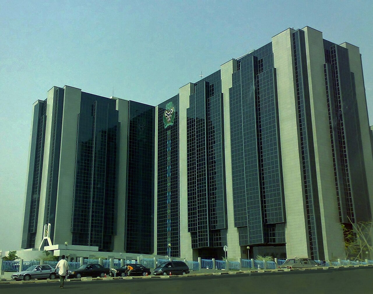 Glass and stone towers of the Central Bank of Nigeria headquarters under a hazy sky in Abuja