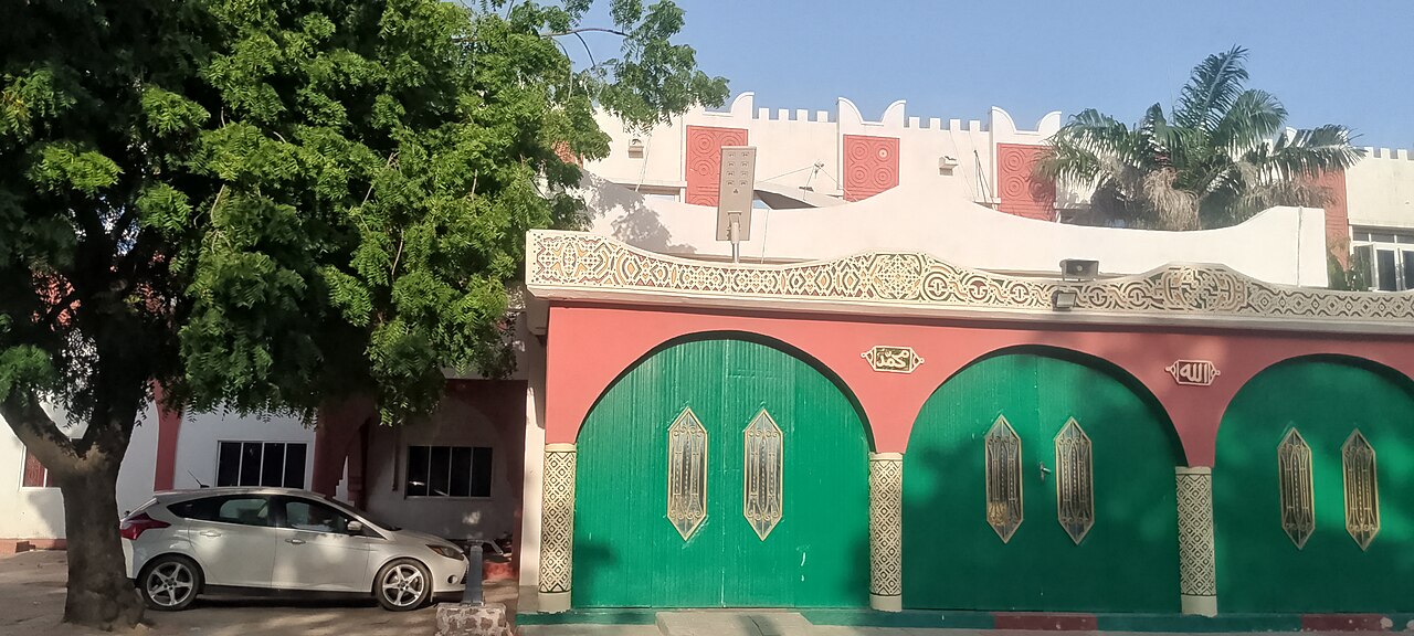 A green-gated building with decorated arches at the Emir of Kano palace, with a tree and a parked car