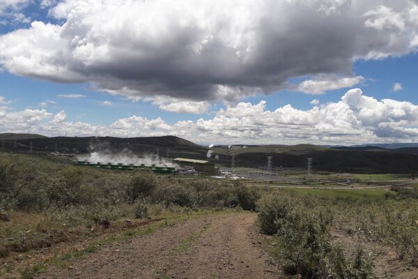 White steam rises from the cooling units of the Olkaria V geothermal power station in Kenya's Rift Valley, with green hills and power lines behind it