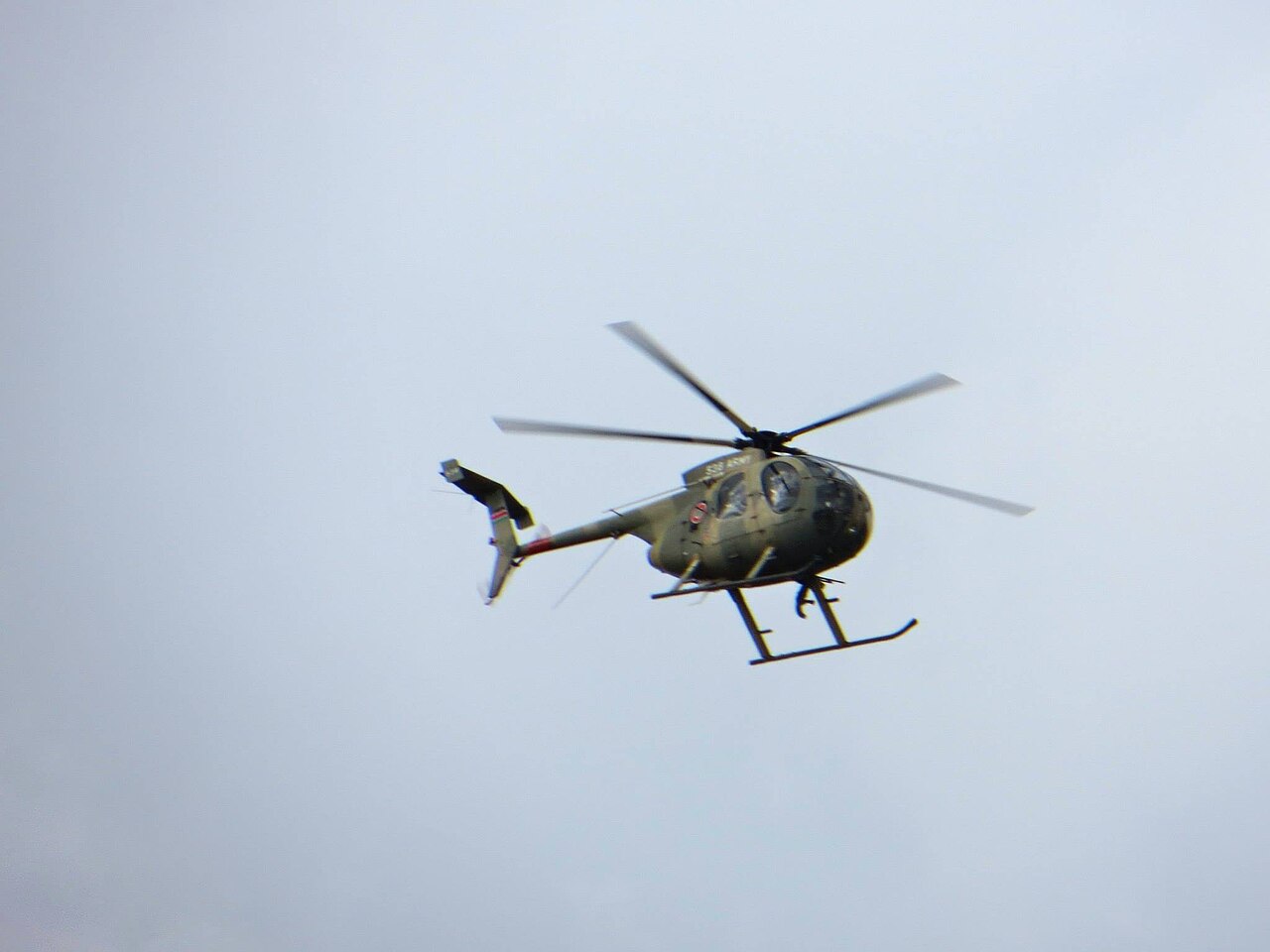 A light olive-green Kenyan Army helicopter with a four-blade rotor flies against a grey sky