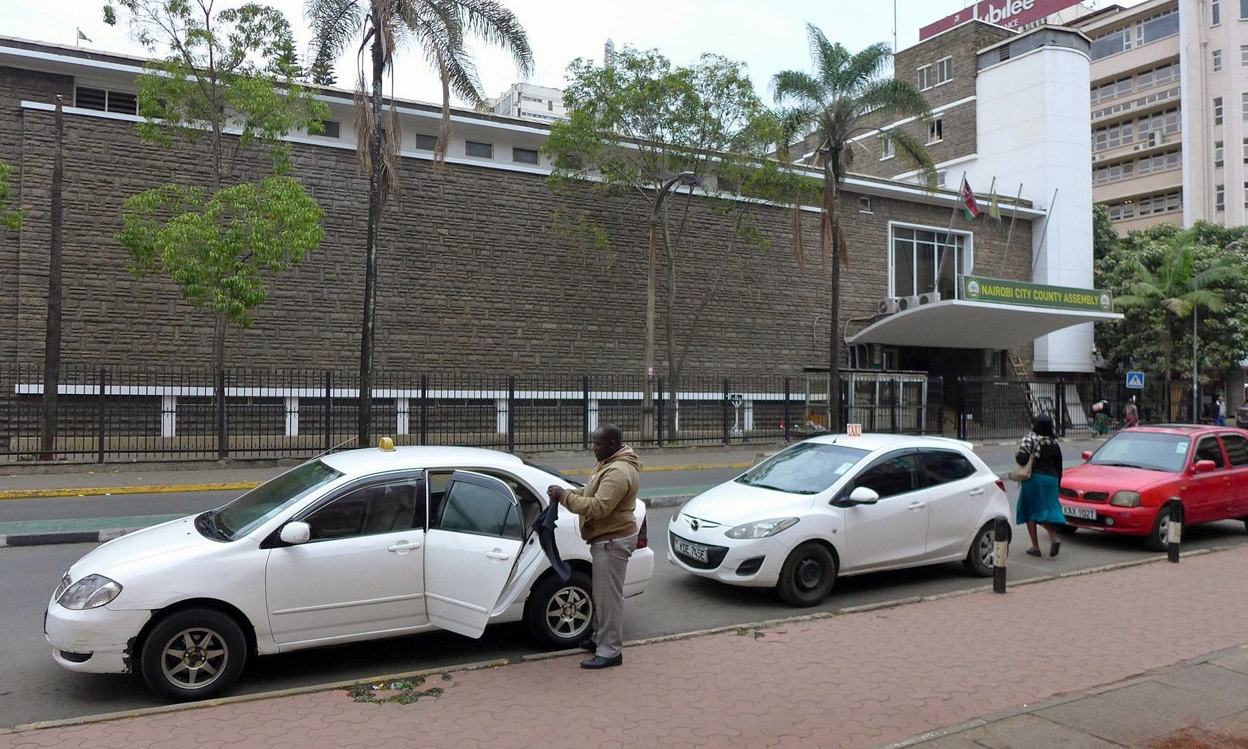 The Nairobi City County Assembly building behind taxis parked on a city street in Nairobi