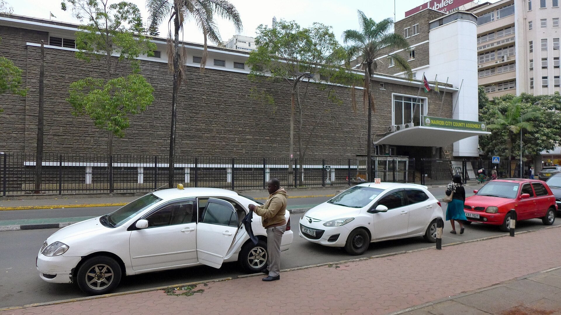 The Nairobi City County Assembly building behind taxis parked on a city street in Nairobi