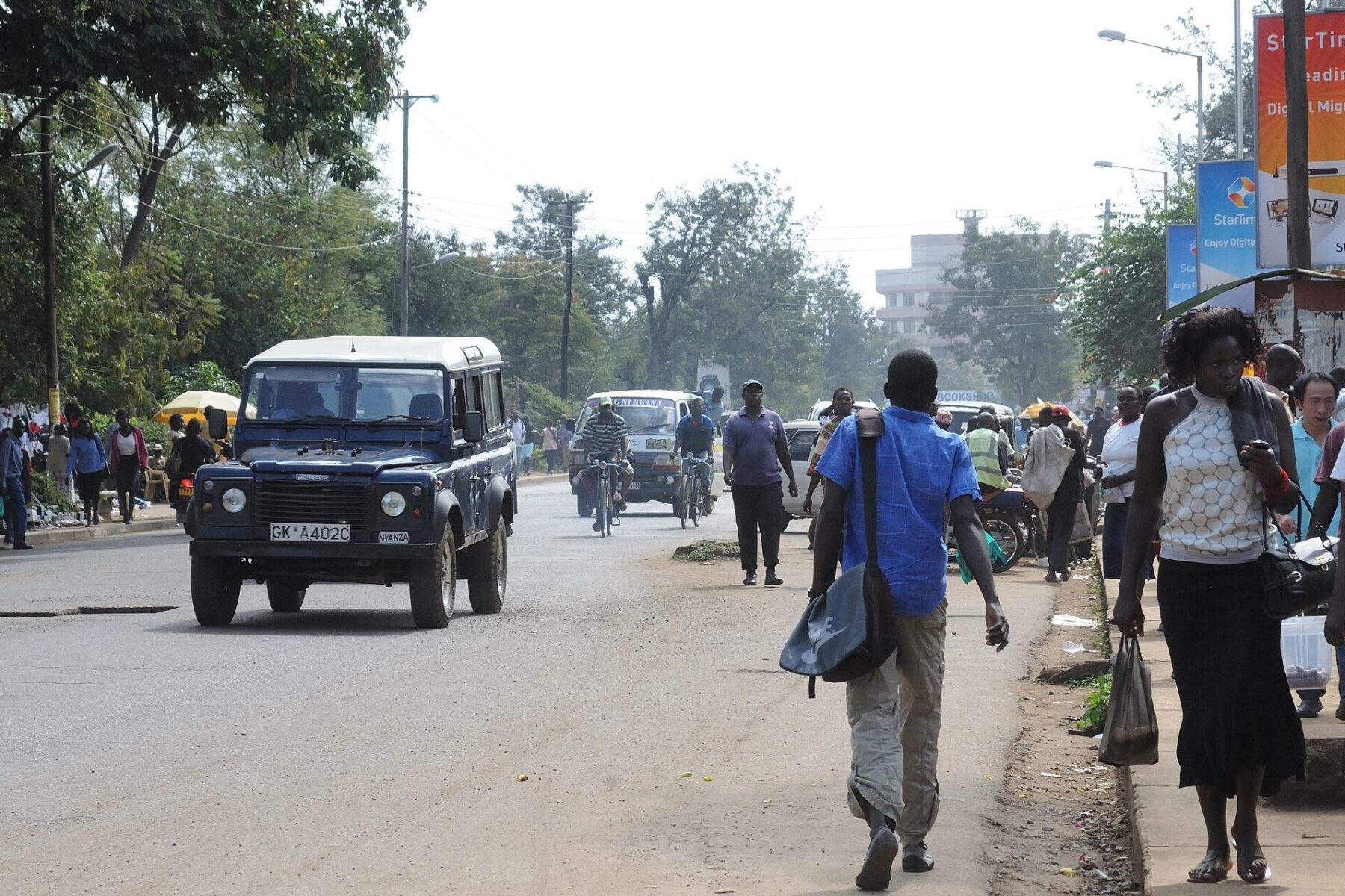 A busy street in central Kisumu with a Land Rover, minibuses, cyclists and pedestrians