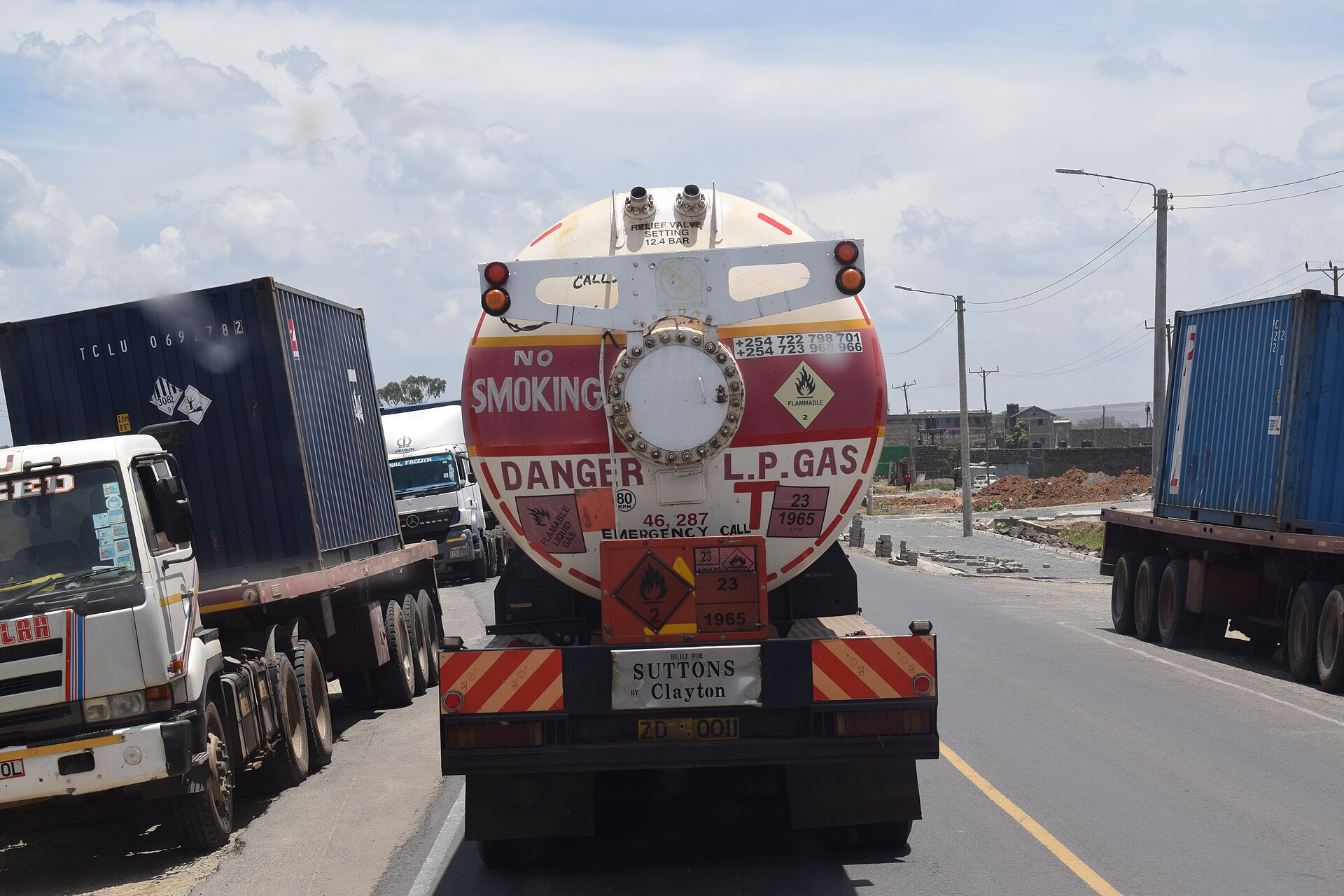 A gas tanker lorry marked with hazard signs in traffic between container trucks on a road in Kenya