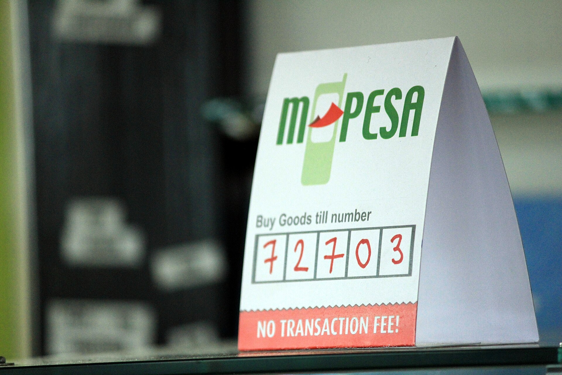 A paper sign on a counter showing an M-Pesa Buy Goods till number and the words No transaction fee