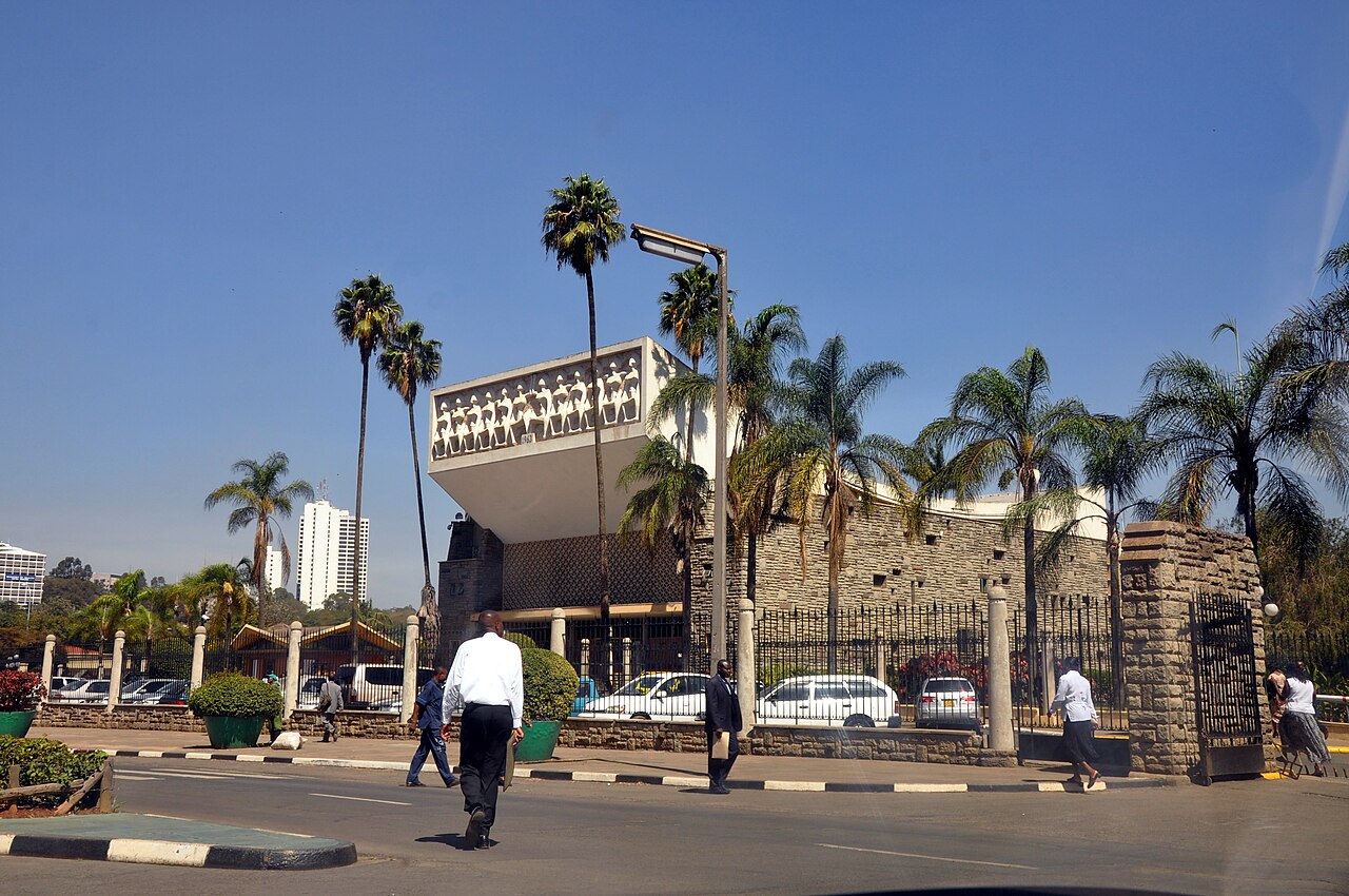 Palm-lined street in central Nairobi with pedestrians and a colonnaded building.