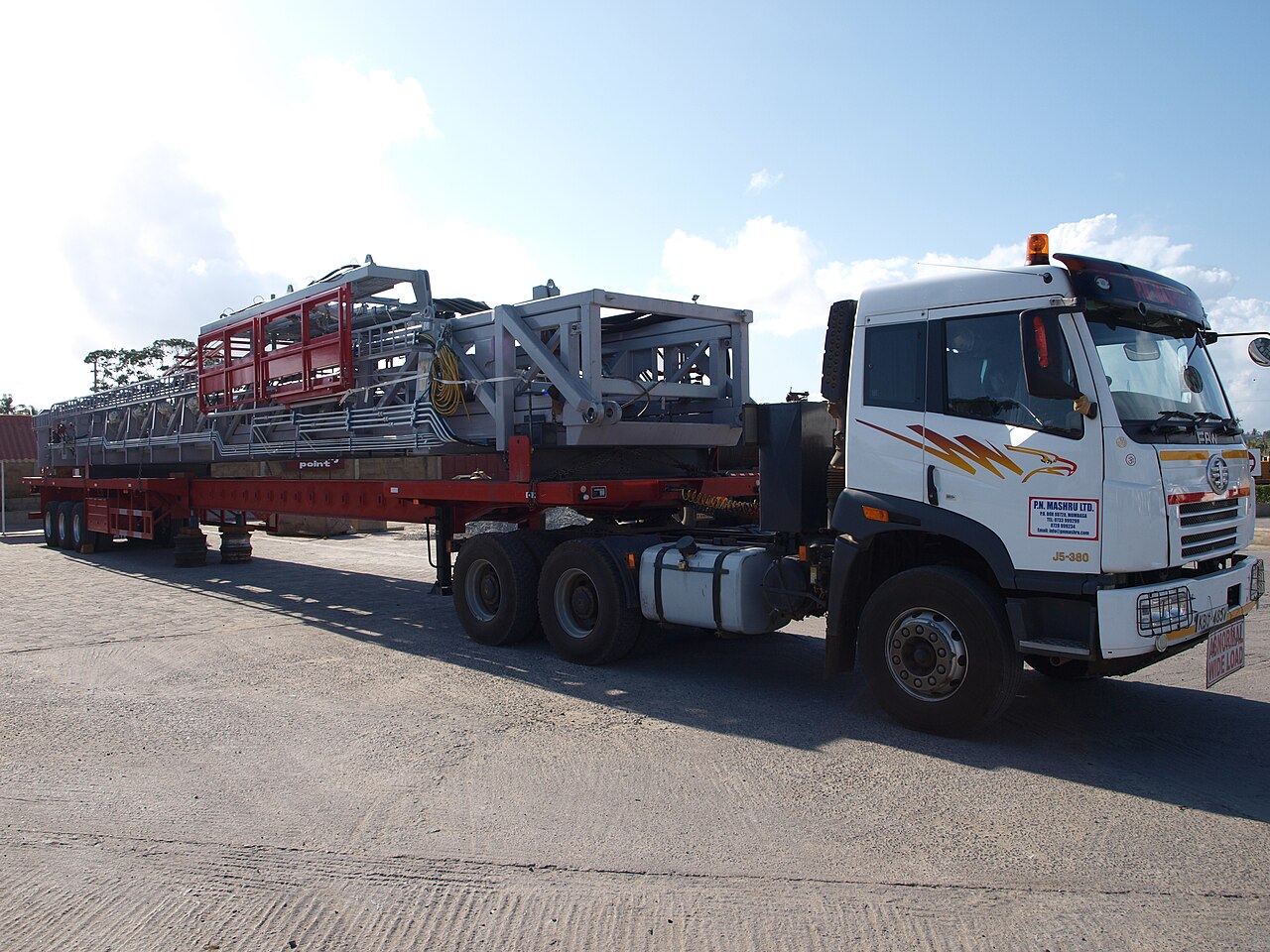 A white truck carries a drilling rig section on a flatbed trailer on a road in Kenya