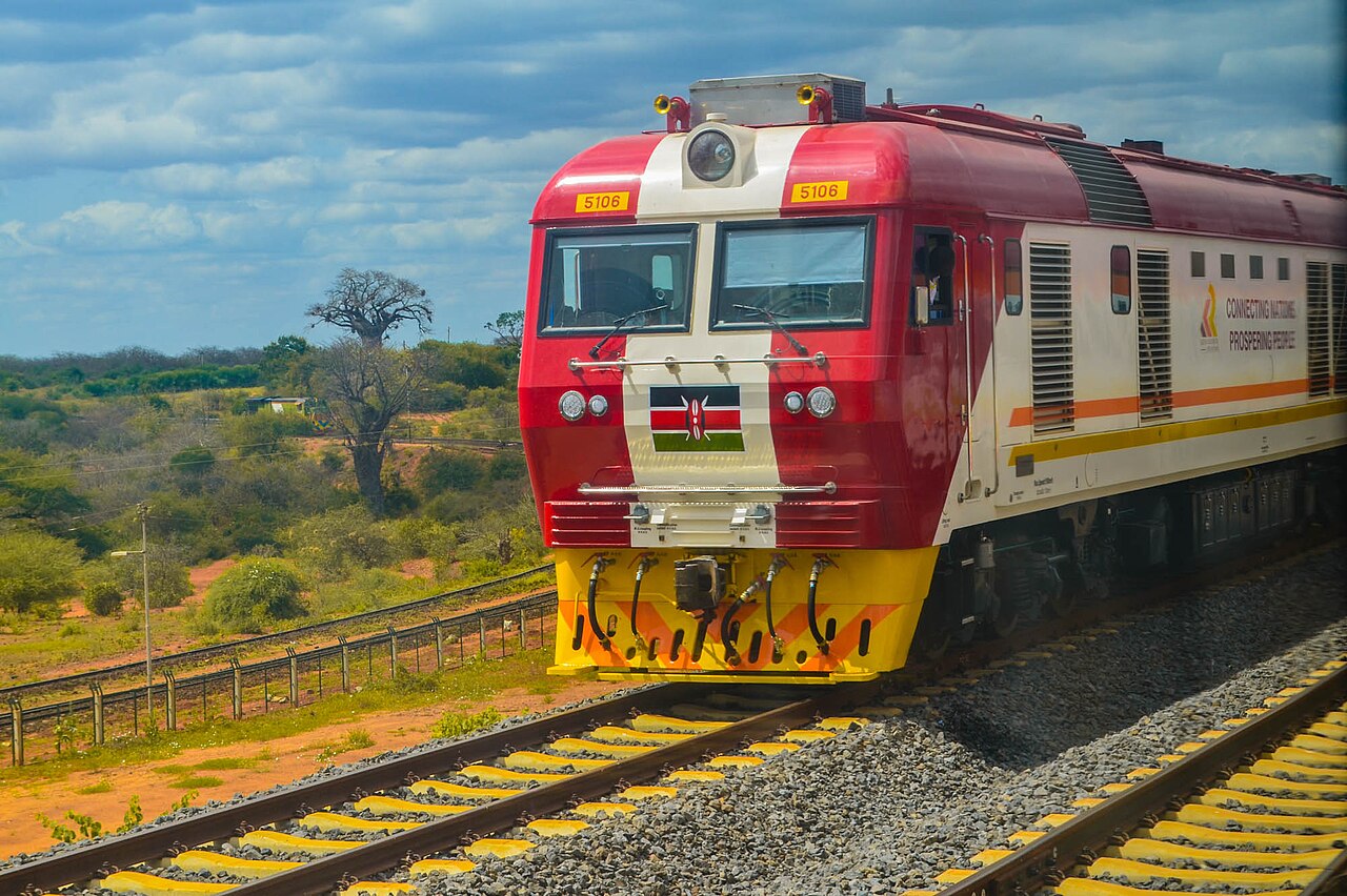 Red and white Kenya Railways locomotive 5106 with the Kenyan flag on its front on the Standard Gauge Railway through dry bush country