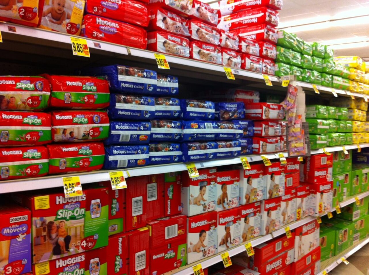 Shelves stacked with red and blue Huggies diaper packs and boxes in a supermarket aisle