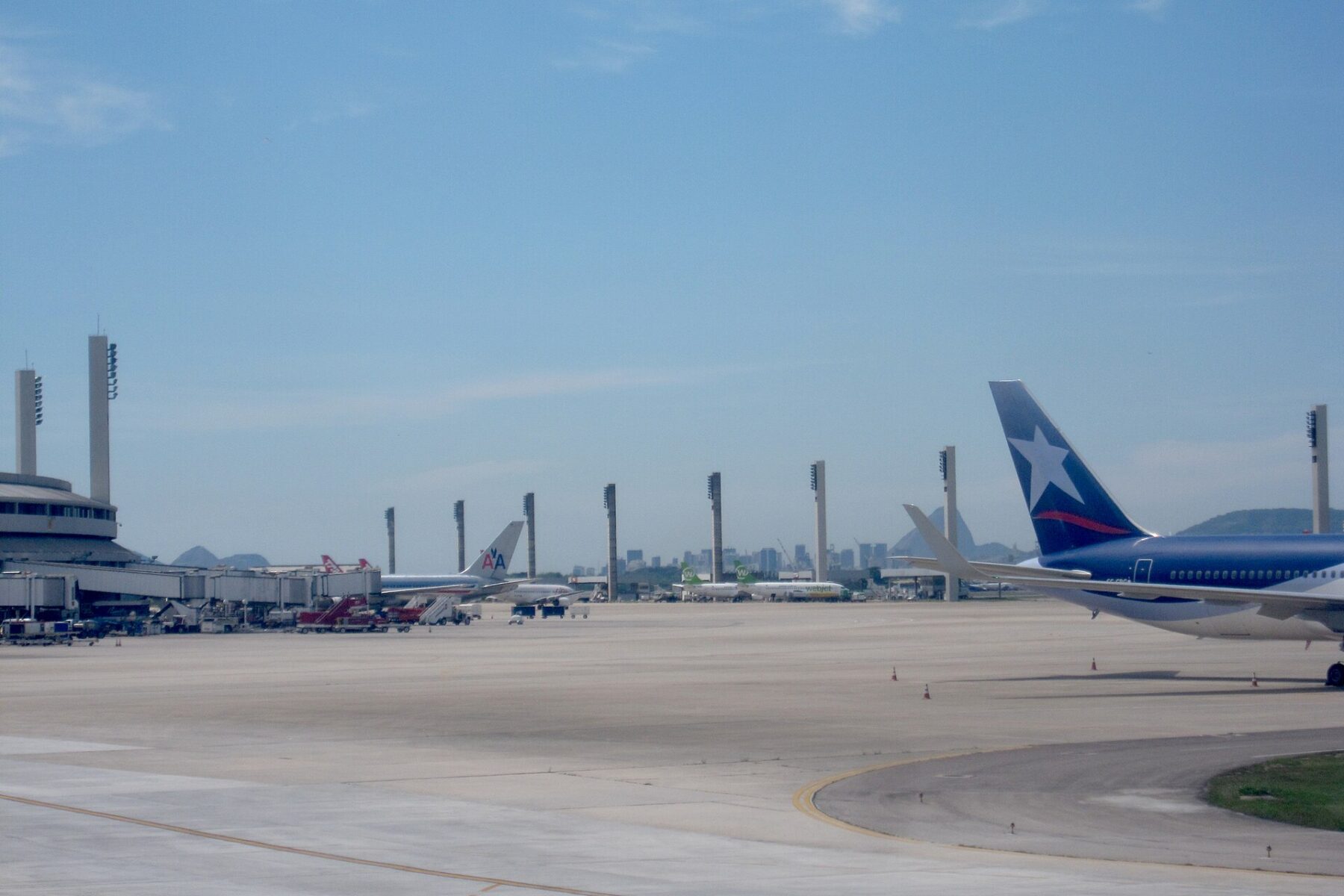 Aircraft parked at the gates of Rio de Janeiro's Galeão international airport, with the control tower and terminal under a blue sky